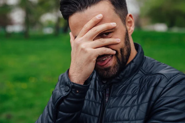 Young man making funny faces and covering his face with a hand.