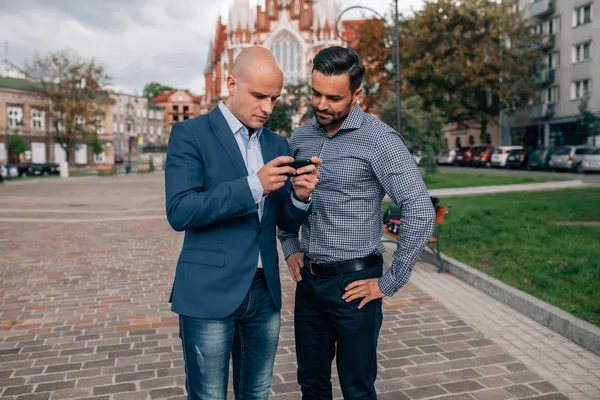 Two elegant men standing with mobile phone.