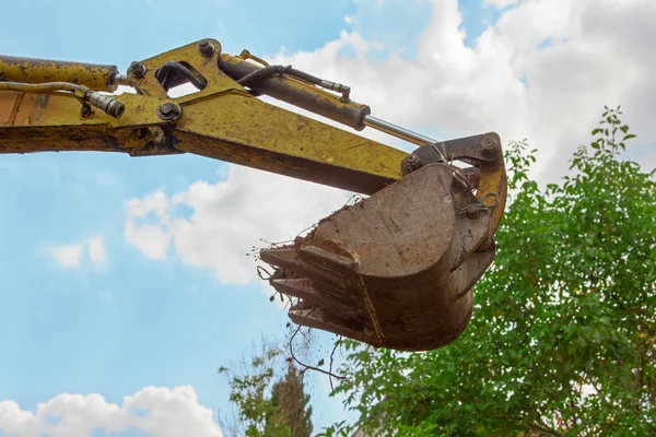 Shovel of a mini digger, blue sky and tree crown