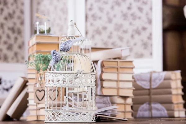 Cage with birds and old books heap in interior rustic decoration