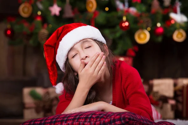 Portrait of cute girl in Santa hat fell asleep under Christmas tree