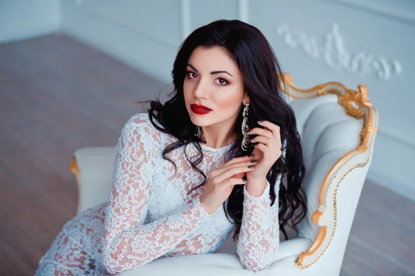 Perfect portrait of sexy young woman with red lips wearing seductive white dress sitting on luxury vintage chair