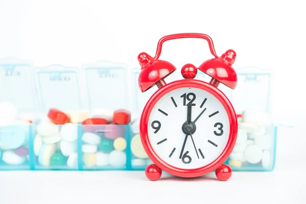Red alarm clock and medicine in weekly pill box