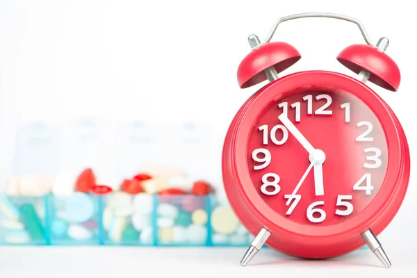 Red alarm clock and medicine in weekly pill box