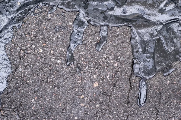 Black bitumen abstract form on damp speckled asphalt