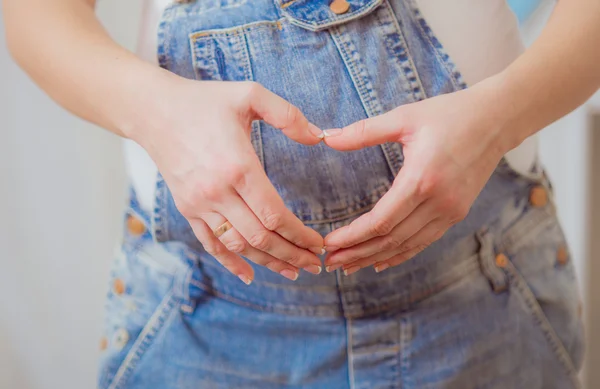 Belly of a pregnant woman in a blue denim overalls