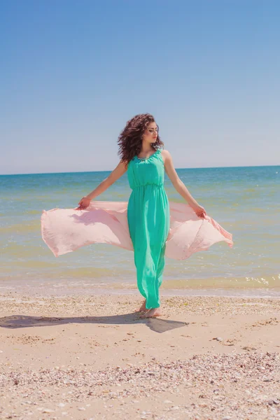Young girl on the beach in summer in a beautiful dress with a flying scarf