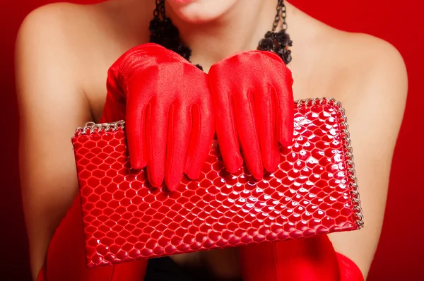 Female hands in red gloves holding a red clutch