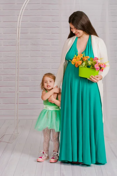 Young pregnant woman in a turquoise dress and little girl