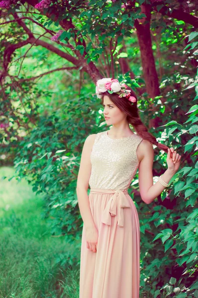 Young beautiful girl in a long dress and a wreath of flowers of lilac bush