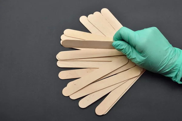 Beauticians hand with green glove holding wooden spatula for wax