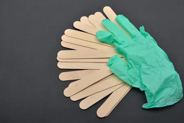 Green glove and wooden spatulas for wax on black. Preparing for