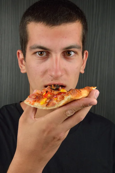 Portrait of a greedy young man eating pizza on a dark background