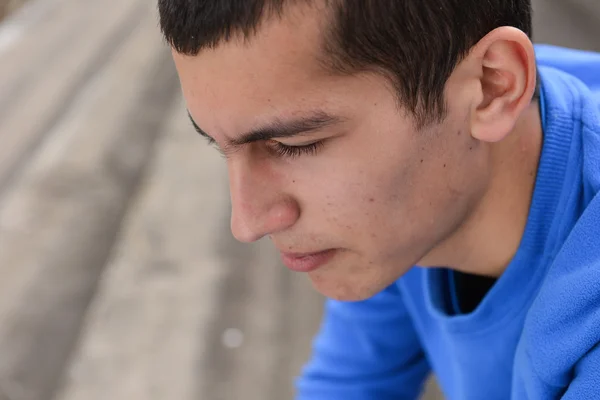 Close up of an unhappy teenage student sitting outside on stadiu