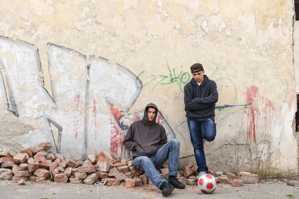 Two street hooligans or rappers sitting against a graffiti paint