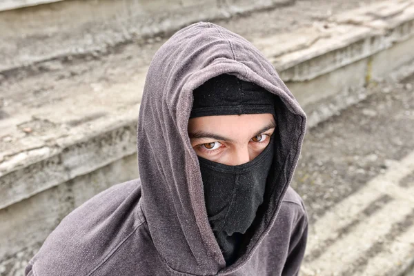 Unrecognizable young man wearing black balaclava sitting on old