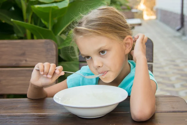 Upset six year old girl slowly eating porridge for breakfast