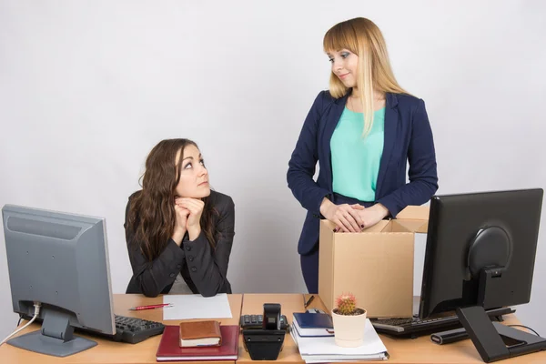 The girl in the office is facing the box with things and looking at the colleague sitting next