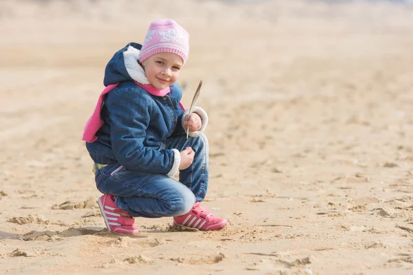 Five-year girl sat down on the sand by the sea with seagulls pen in hand