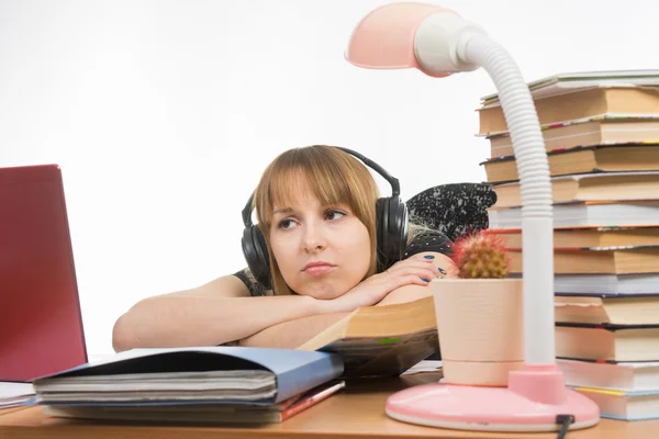 Girl sad student sitting at the table wearing headphones and listening to music