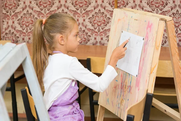 Girl paints on an easel in the drawing lesson