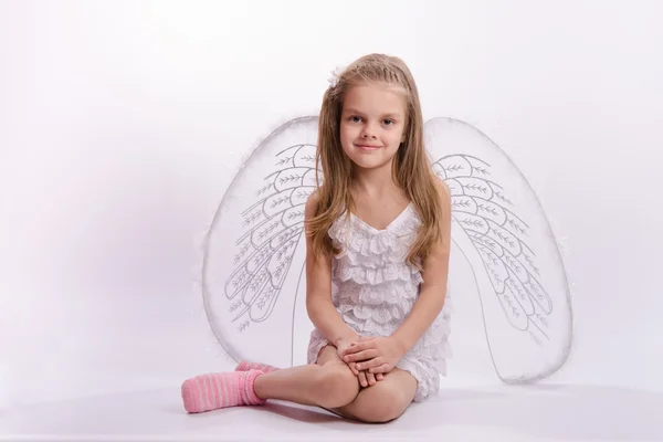 Sitting girl in an angel costume on a white background