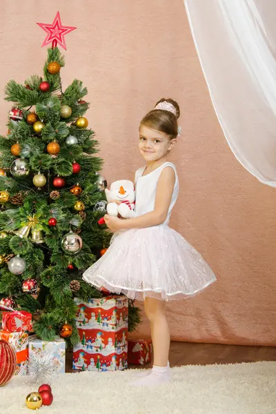Five-year girl standing with toy snowman at Christmas tree