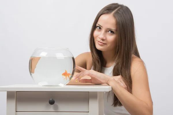 The girl points a finger at aquarium with goldfish