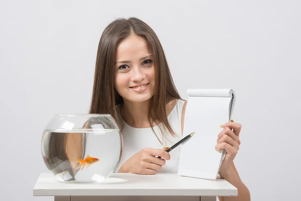Girl shows a pen entry pad, standing next to an aquarium with goldfish