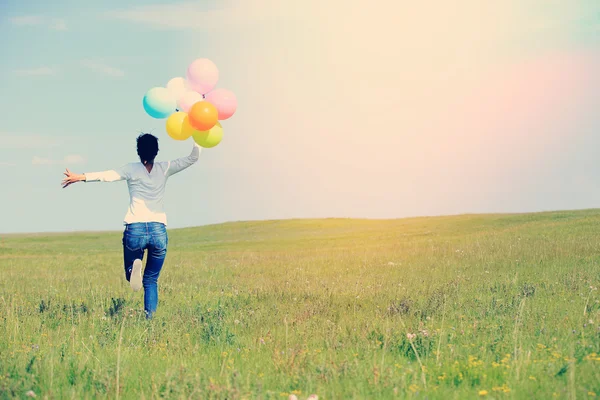 Young asian woman running and jumping on green grassland with colored balloons