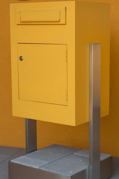 Yellow post box stands on concrete base