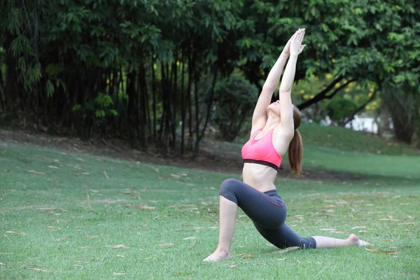 Woman practicing Warrior yoga pose outdoors on lawn