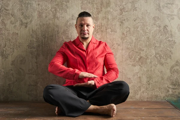 Portrait of a young man, in red shirt and black slacks, hairstyle with shaved temples and slicked back hair at the head, different emotions, wood floor, beard, lotus posture, beige wall with drawings