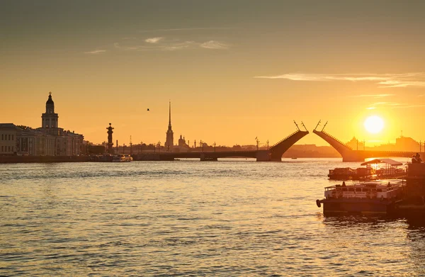 Russia, Saint-Petersburg, 03 July 2016: Closing of Palace Bridge at sunrise, the Peter and Paul Fortress Spike in the orange sky, Rostral colomn, ships, boats, the traffic beginning, sun,