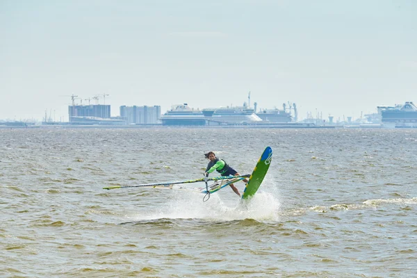 Russia, St. Petersburg, 07.04.2015: prorider Yegor Popretinsky, rus11, Russian champion in windsurfing performs a trick SHAKA, against the backdrop of the city of St. Petersburg Marine Port, ferry ships, the Gulf of Finland