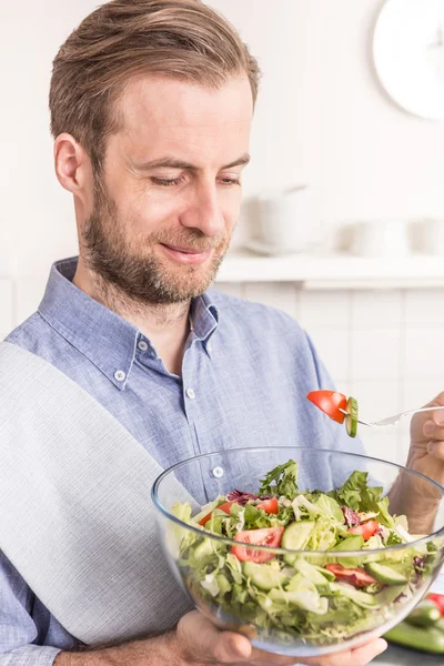 Happy smiling man eating fresh vegetable salad in the kitchen