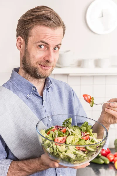 Happy smiling man eating fresh vegetable salad in the kitchen