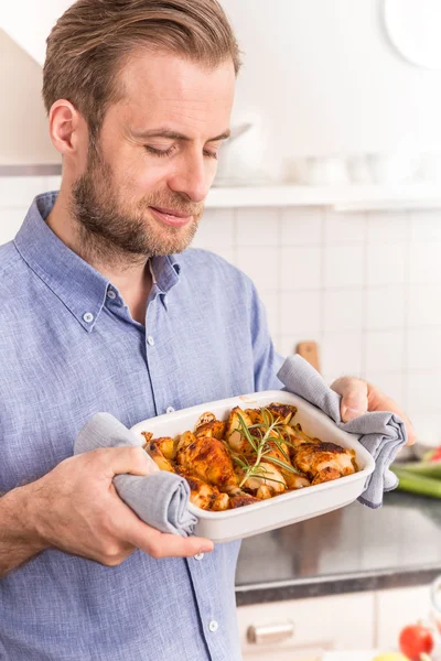 Man or chef holding roasting dish with hot chicken drumsticks