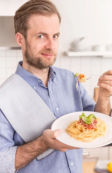 Happy smiling man eating spaghetti bolognese in the kitchen