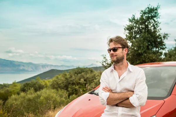 Man (driver, tourist) in front of a car and landscape