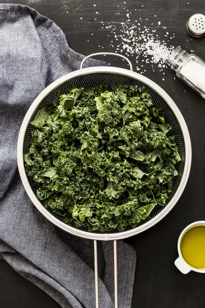 Fresh wet kale in a sieve and grey napkin on black