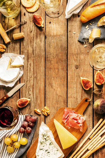 Different kinds of cheeses, wine, baguettes, fruits and snacks