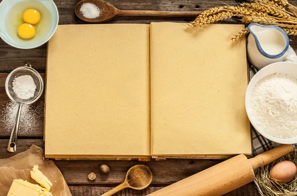 Blank cook book and baking cake ingredients on wood