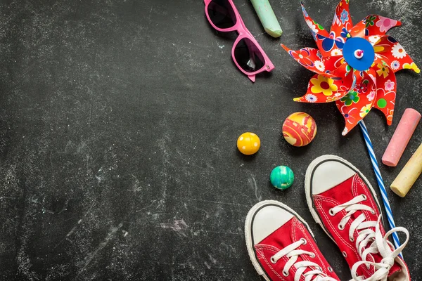 Toys and red sneakers on black chalkboard - top view