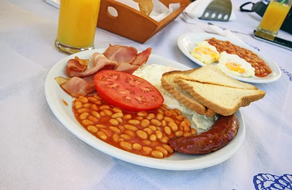 Full English cooked breakfast with bacon, sausage, fried egg and baked beans .