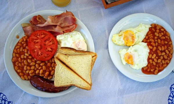 Full English cooked breakfast with bacon, sausage, fried egg and baked beans .