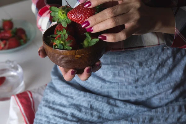 Woman sitting with bowl of strawberries in hand.