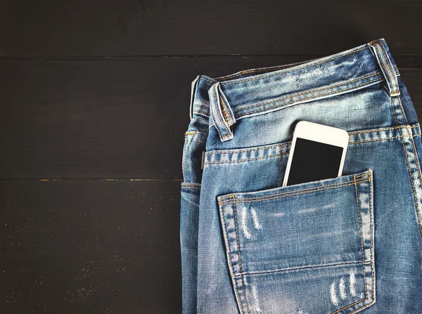 Jeans and mobile phone on wooden boards.