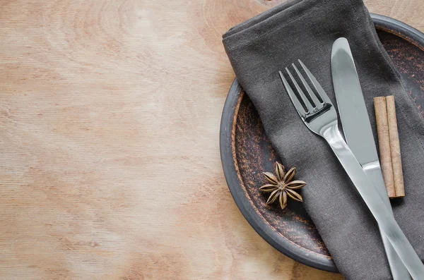 Table setting with a plate, cutlery and napkin in brown colors.