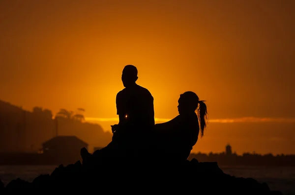 Silhouette of man and women against sunset over a harbor